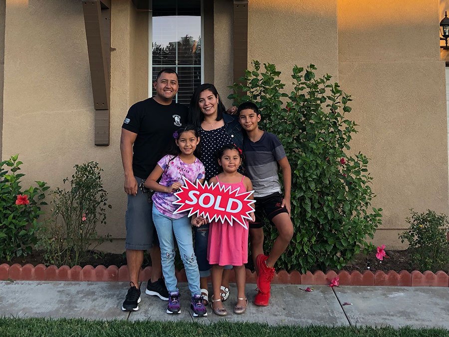 Man, Woman and three children standing in front of a home, holding a sign that says sold.